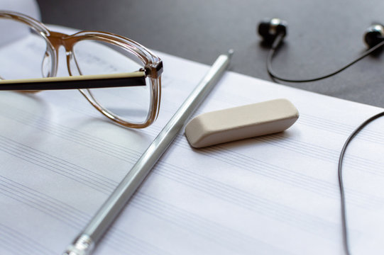 Side view of the gray pencil, eyeglasses, black earphones and eraser laying on the sheet notes with handwritten notes. The concept of the music creating, composing, note writing, music art.