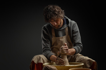 A male potter works with clay on a potter's wheel.