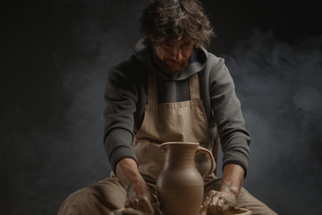 A male potter works with clay on a potter's wheel.