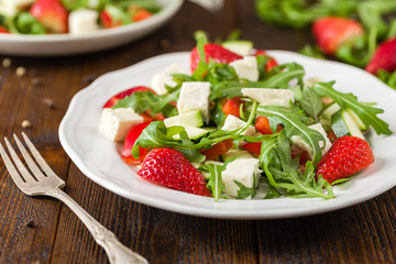 Fresh vegetable strawberry salad on white plate on natural rustic desk.