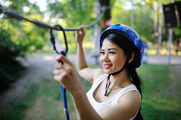 Asian girl in a helmet and special equipment for rock climbing with safety carbine in hand passes...