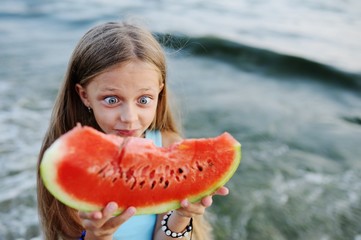 baby girl in the hat eagerly eats juicy watermelon on sea background