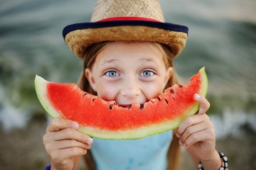 baby girl in the hat eagerly eats juicy watermelon on sea background