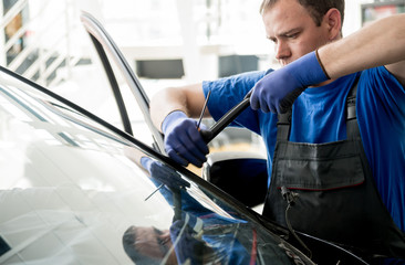 Automobile special workers remove old windscreen or windshield of a car in auto service station...