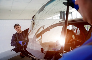 Automobile special workers remove old windscreen or windshield of a car in auto service station...