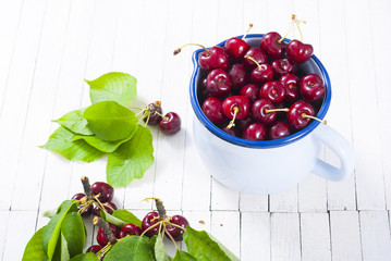 Cherry in old enamel mug, white wood table background