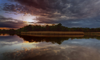 Beautiful sunset over lake with reflection in water, majestic clouds in the sky Toned Image