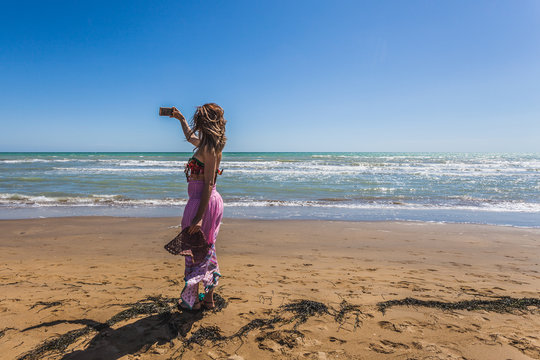 Girl on a beach making photos with phone in a windy morning, Bibione beach, Venice, Italy