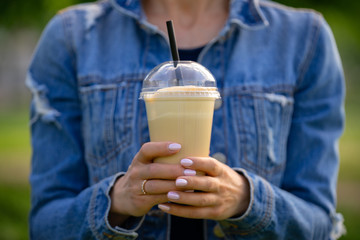 Cool young woman in denimm clothes with takeaway frappe coffee