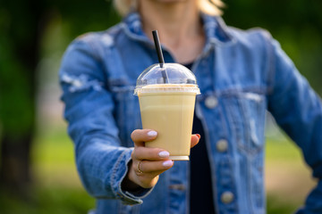 Cool young woman in denimm clothes with takeaway frappe coffee