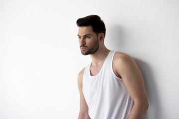 Handsome and confident. Young attractive man is standing against light wall while looking aside thoughtfully. Copy space in the left side