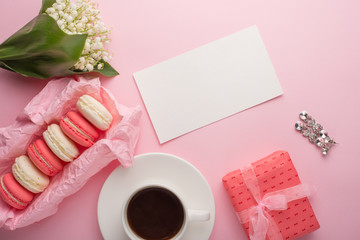Flatlay with macaroons, flowers and a gift with female earrings and an empty place for inscription on a light pink background. Can be used as a postcard for a holiday