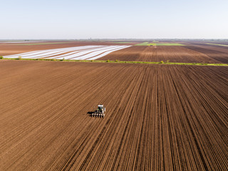 Obraz premium Aerial shot of a farmer seeding, sowing crops at field. Sowing is the process of planting seeds in the ground as part of the early spring time agricultural activities.