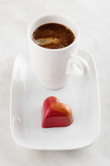 Red heart shaped handmade chocolate candy on plate with cup of coffee espresso