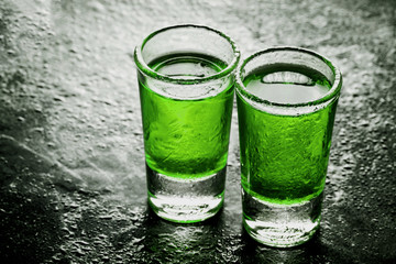 Two glass vodka shots with abstract color green alcohol poured inside. Weekend alcohol party background.