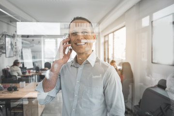 Portrait of happy male talking by phone while looking at window. Cheerful worker with gadget concept