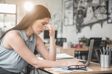 Side view sad businesswoman feeling pain in eyes while typing in laptop in office. Sick worker at...