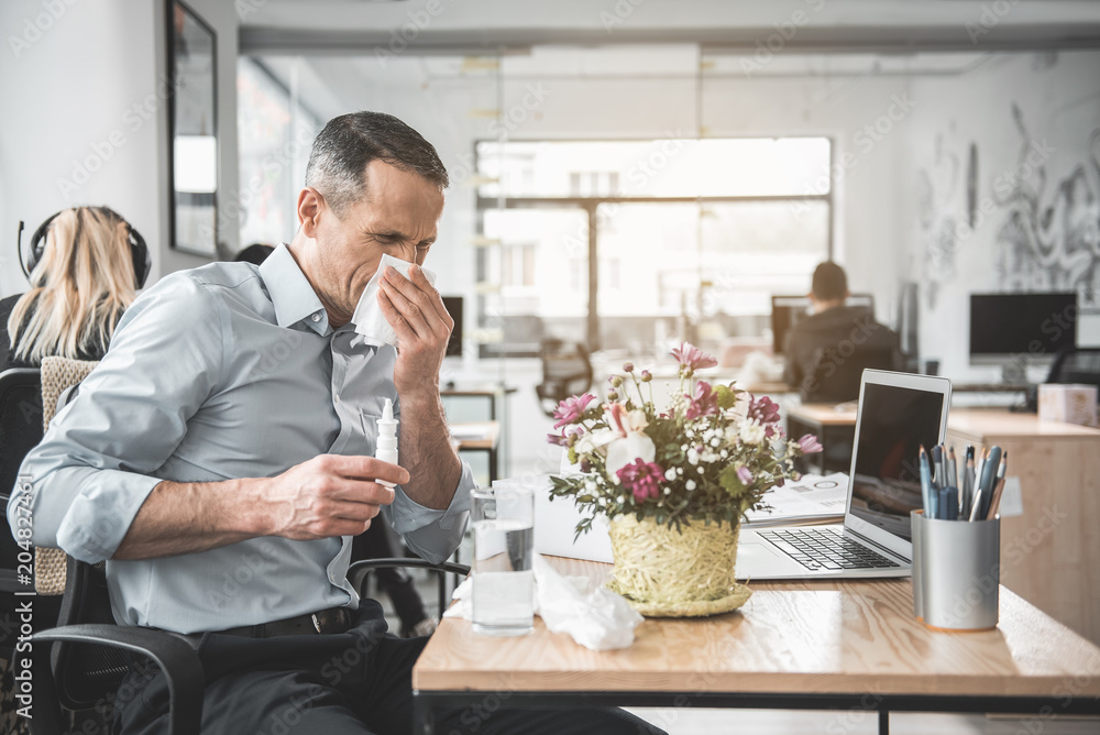 Poster side view frustrated businessman blowing nose into handkerchief while using notebook computer. unhap