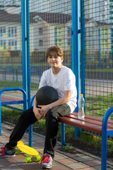 cute young  teenage  boy playing basketball outdoors preparing for shooting, drinks water on sports ground after game