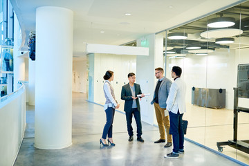 Full length portrait of group of young business people standing in modern office building discussing project, copy space