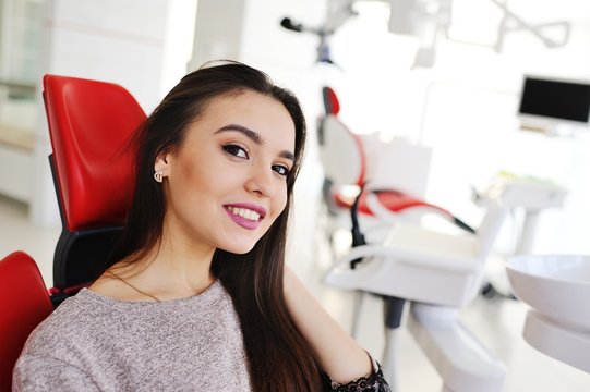 Beautiful, young brunette girl in red dental chair smiling