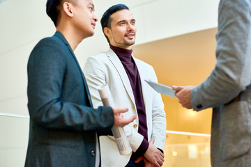 Portrait of handsome businessman discussing collaborative project with colleagues standing in hall of modern office building, copy space