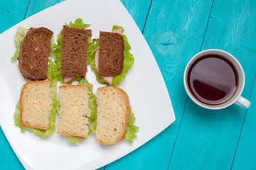 Bruschetta of white and black bread lay on a plate. The dish of sandwiches standing on the wooden surface. A Cup of tea next to a plate of sandwiches. Flat lay of food