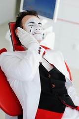 A male mime or clown in a dental chair suffers from a toothache. Caries, sick tooth, dental nerve