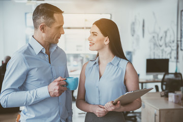 Fototapeta premium Side view happy male talking with outgoing girl while drinking cup of coffee. Glad employers at job concept