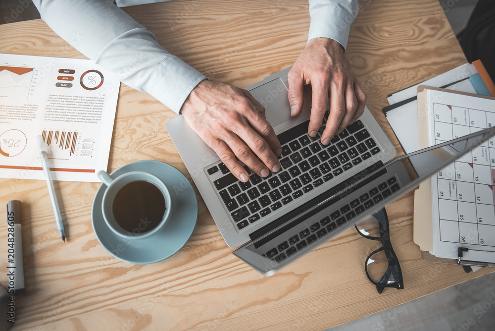 Poster top view close up male hands typing in notebook computer. it locating on desk near mug of beverage