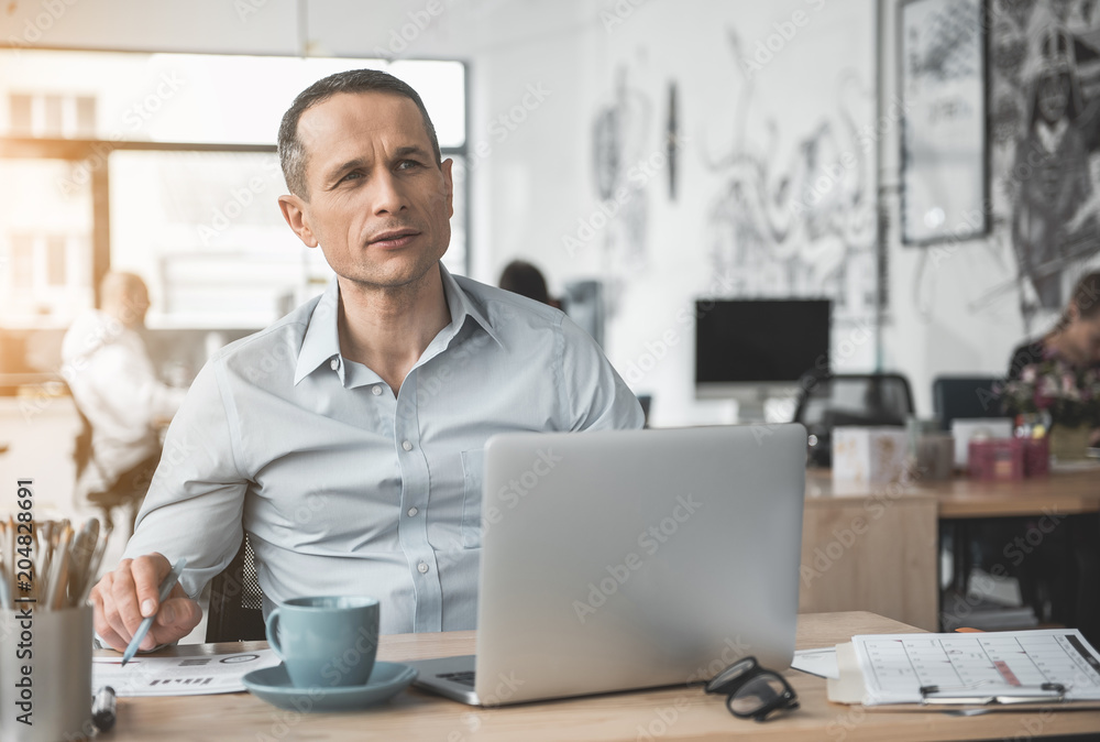 Poster Pensive businessman reading document while typing in notebook computer. He locating at table. Wistful worker at job concept