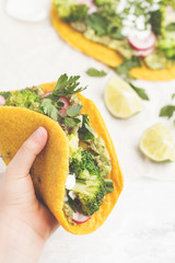 Vegan turmeric tacos with radish, broccoli and guacamole in hand. Healthy vegan food concept.