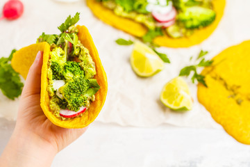 Vegan turmeric tacos with radish, broccoli and guacamole in hand. Healthy vegan food concept.