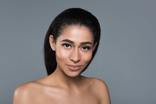 Portrait of smiling woman with nude shoulders staring at camera. Her skin is sleek and glossy. Copy space in right side. Isolated on background
