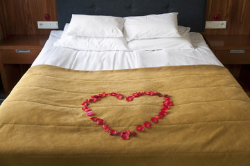 Heart from rose petals on a bed