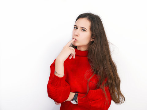 Young beautiful brunette woman in red sweater showing suspicious emotion posing against white background