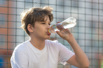 cute young  teenage  boy playing basketball outdoors preparing for shooting, drinks water on sports ground after game