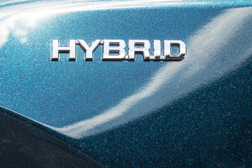 Close-up side view of modern hybrid car. HYBRID  symbol on metallic shiny car fender. Green eco...
