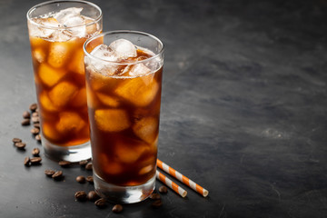 Ice coffee in a tall glass over and coffee beans on a old rustic wooden table. Cold summer drink on a dark background with copy space