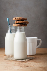 A stack of cookies with milk chocolate and two bottles of milk on a wooden table