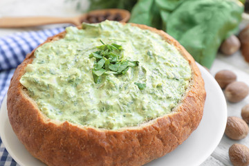 Bread loaf filled with tasty spinach sauce on table