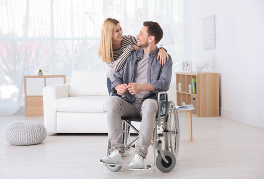 Young woman taking care of man in wheelchair indoors