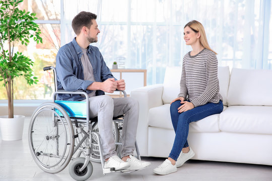 Young woman talking to man in wheelchair indoors