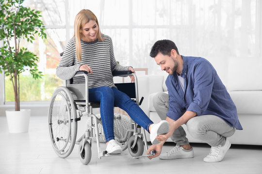 Young man taking care of woman in wheelchair indoors