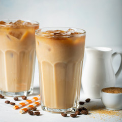 Ice coffee in a tall glass with cream poured over and coffee beans. Cold summer drink on a light blue background