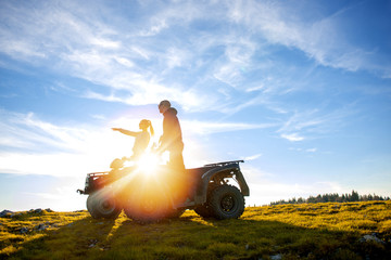Beautiful couple is watching the sunset from the mountain sitting on atv quadbike © FS-Stock