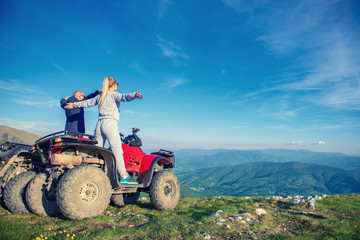 Beautiful couple is watching the sunset from the mountain sitting on atv quadbike