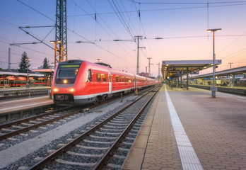 High speed red train on the railway station at sunset. Nuremberg, Germany. Colorful urban...