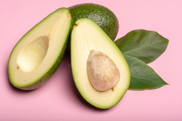 Fresh organic ripe green whole and sliced Fuerte avocado with leaves, copy space close up isolated on trendy pink background