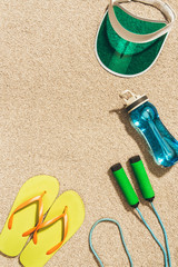 top view of arranged cap, flip flops, water bottle and jump rope on sand